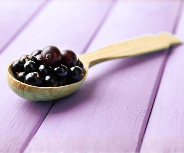 Wooden spoon filled with blackcurrants on a purple wooden surface