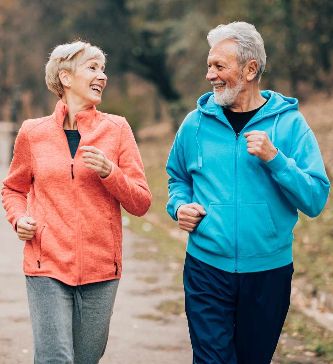 Two elderly people jogging outdoors in colorful jackets.