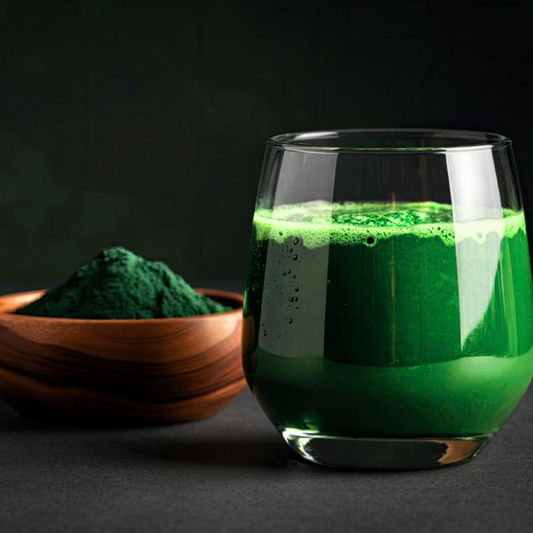 Glass of green liquid next to a bowl of green powder on a dark background